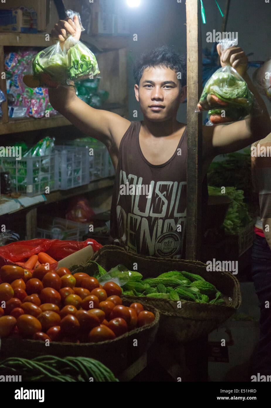 Bali, Indonesia.  Young Man Offering Bags of vegetables for Sale.  Jimbaran Market. Stock Photo