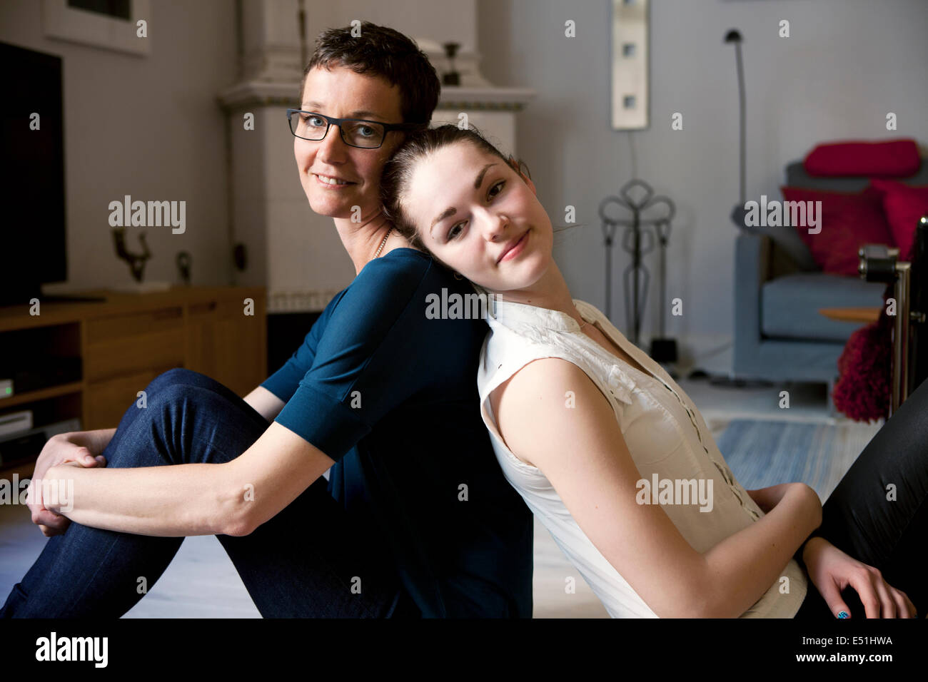 Portrait of mother with daughter (16-17) sitting on floor back to back Stock Photo