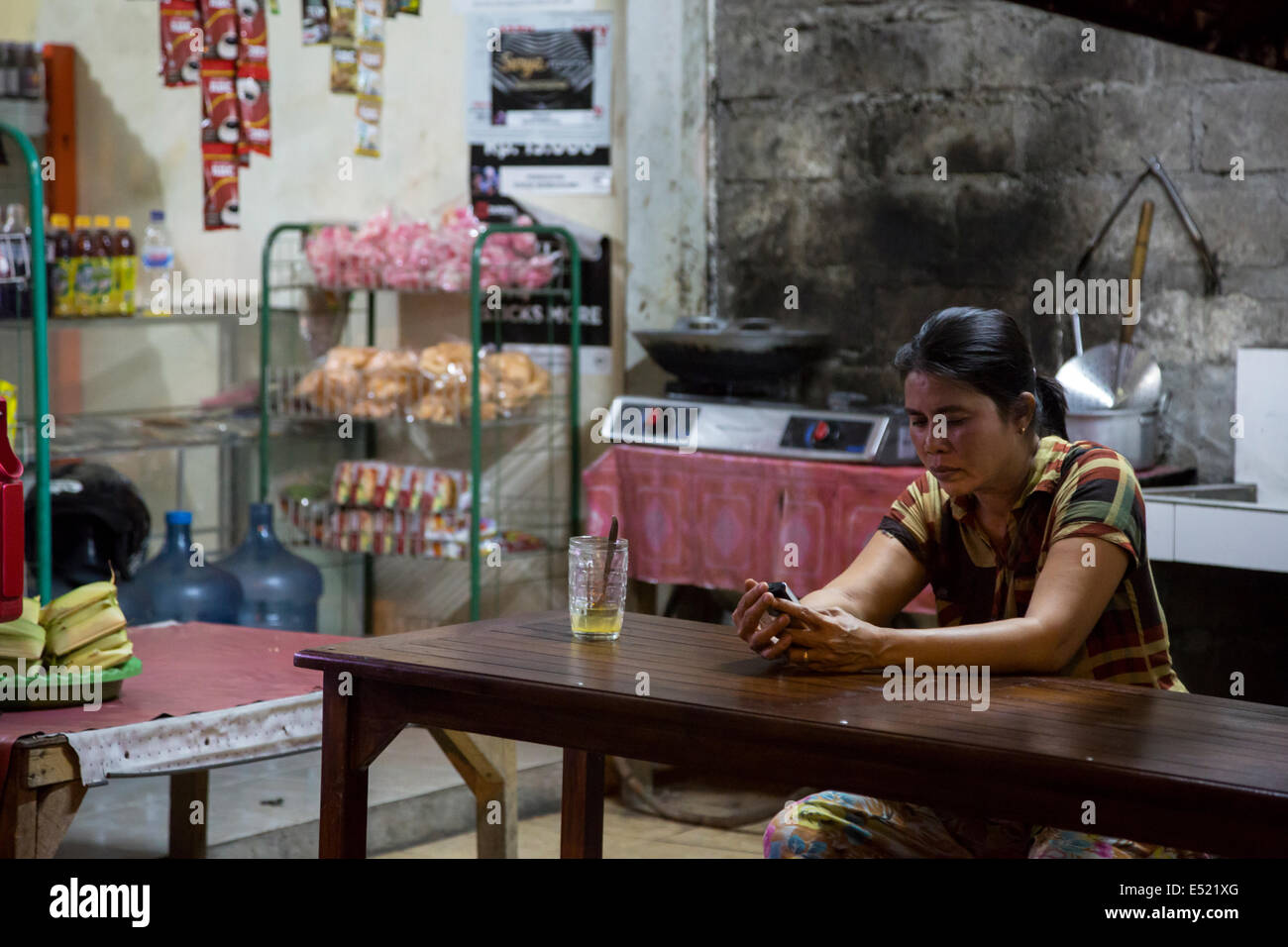 Jimbaran, Bali, Indonesia.  Woman Checking her Cell Phone at a Nighttime Refreshment Shop. Stock Photo