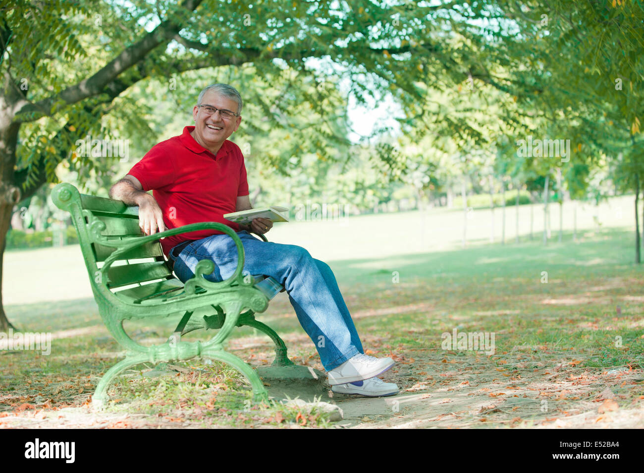 Senior man with a book sitting on a bench Stock Photo