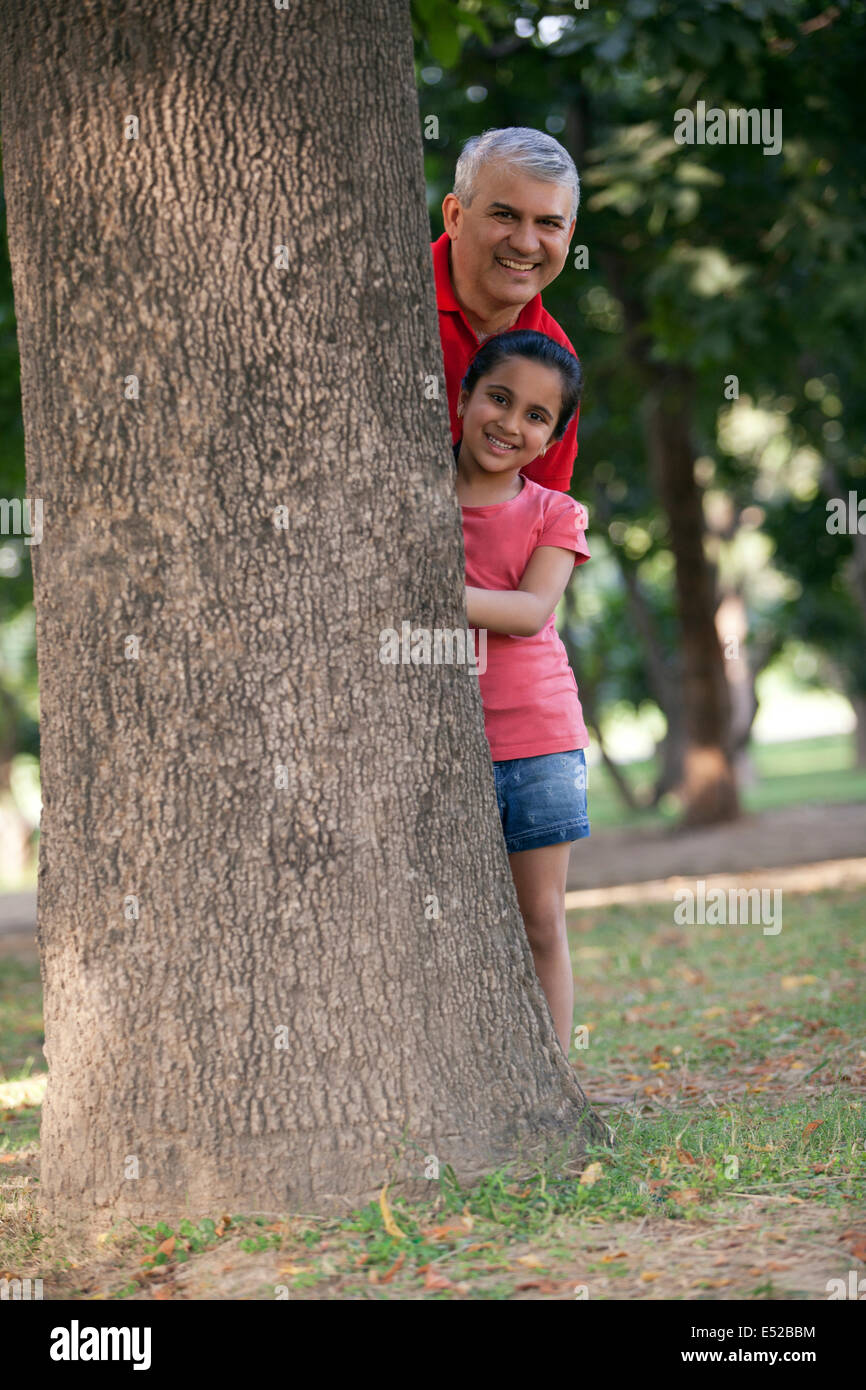 Portrait of grandfather and granddaughter standing behind tree Stock Photo