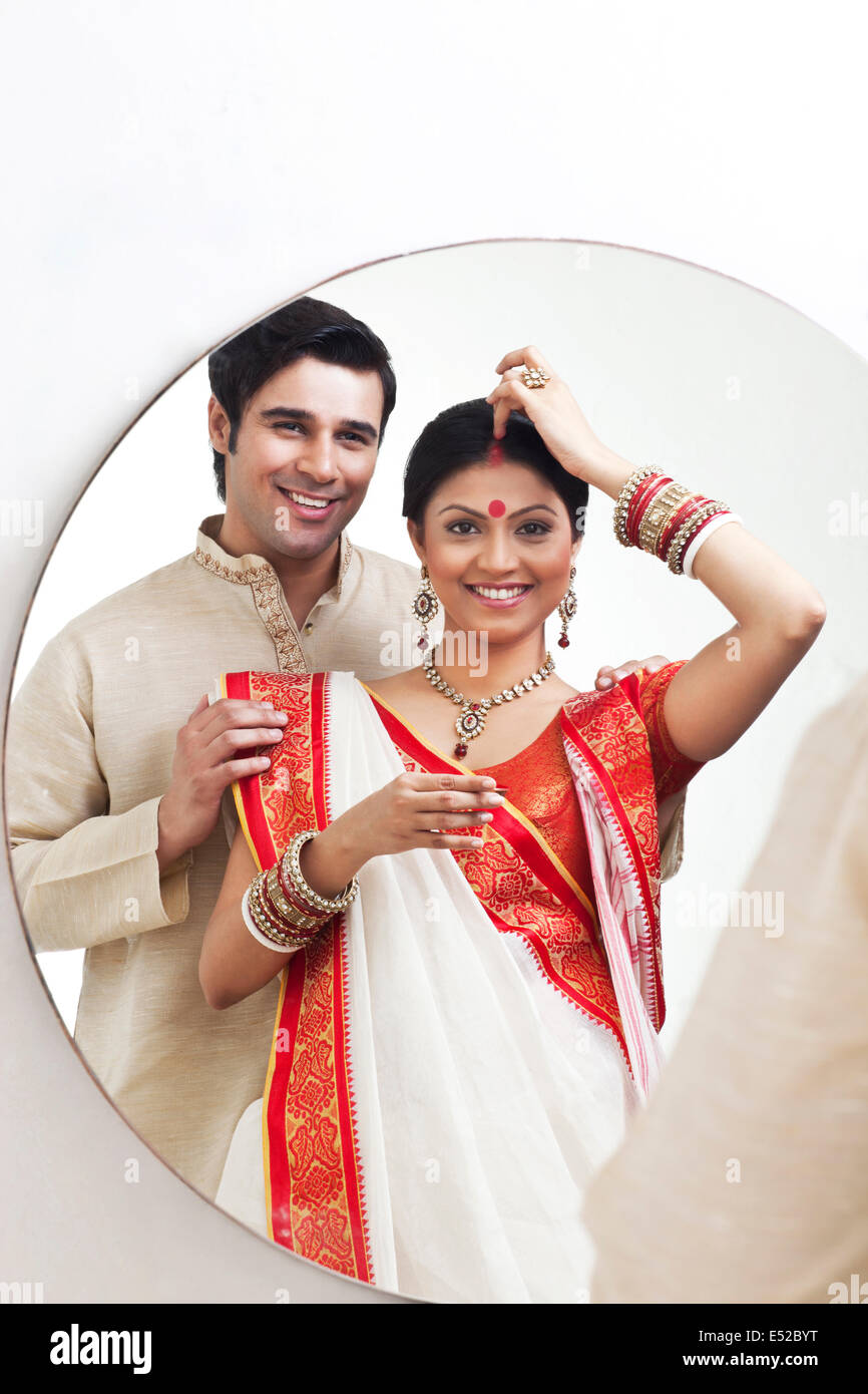 Bengali woman putting sindoor on her forehead while husband watches on Stock Photo