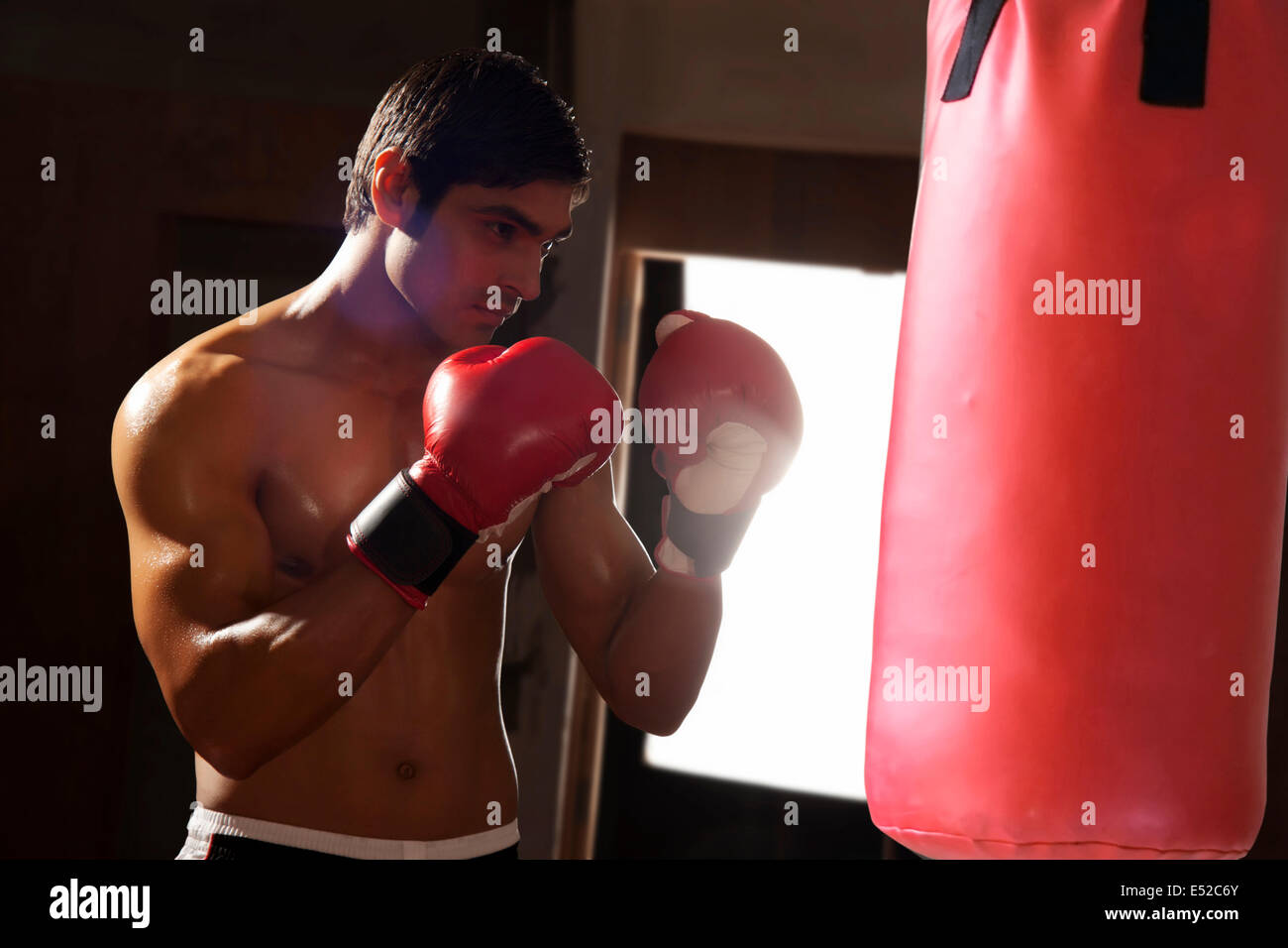Young shirtless man working out with punching bag in gym Stock Photo