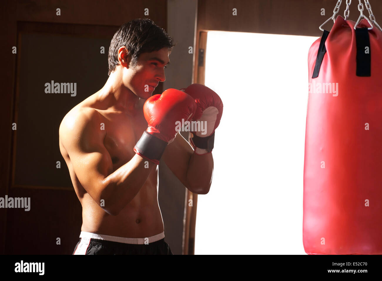 Young shirtless man working out with red punching bag in gym Stock Photo