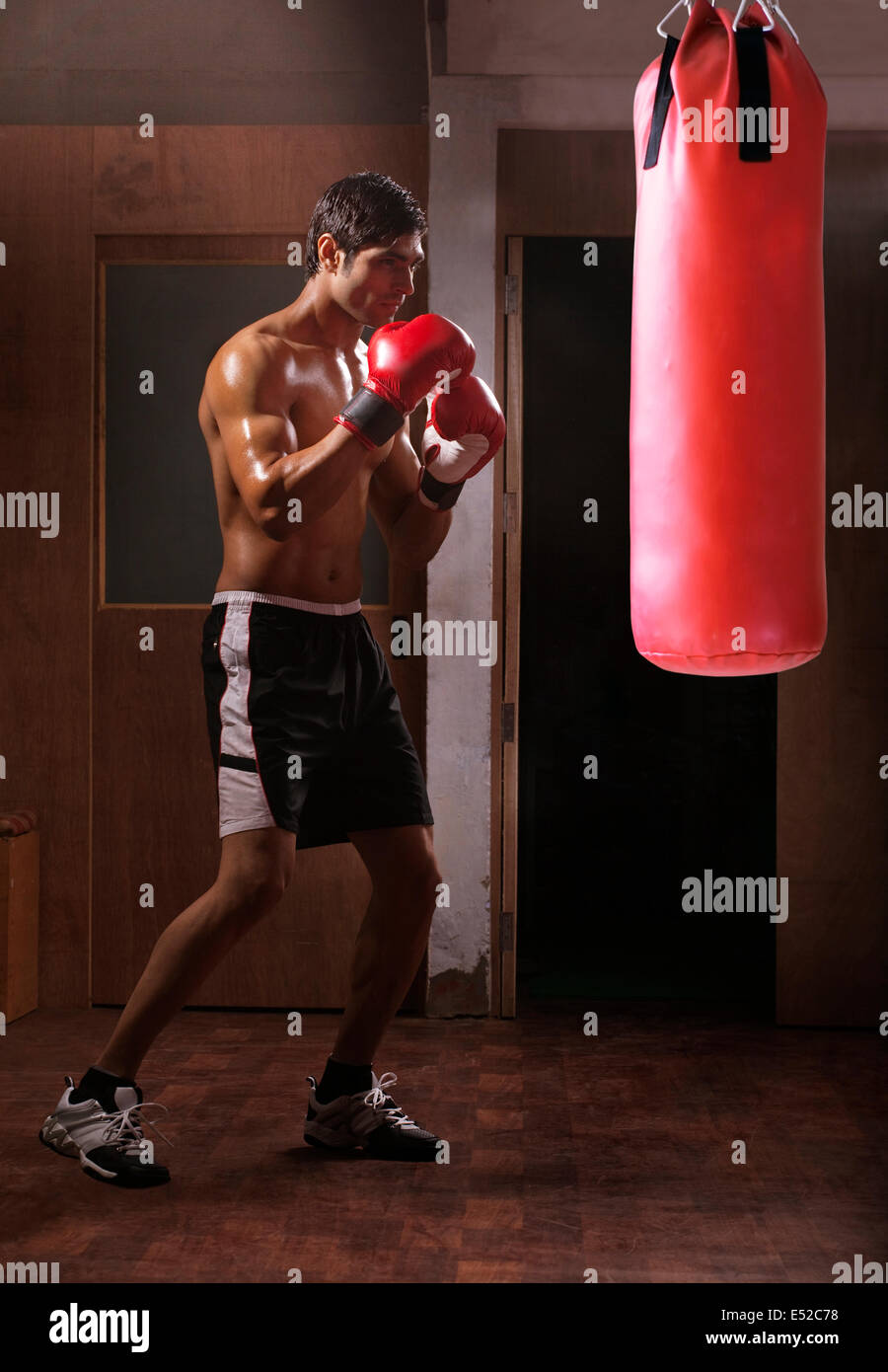 Full length of young shirtless man working out with punching bag in gym Stock Photo