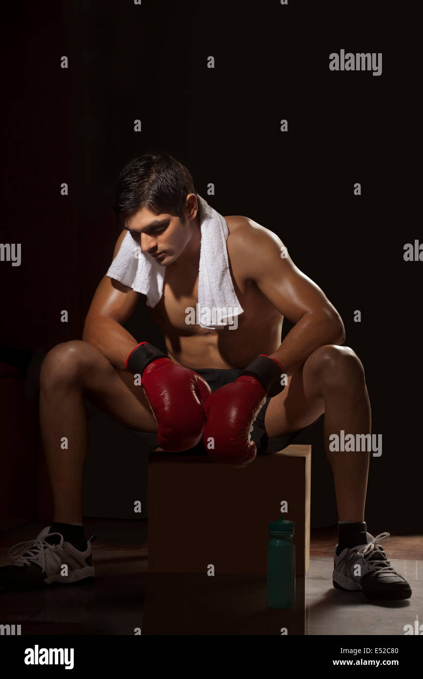 Tired man wearing boxing gloves resting on stool at gym Stock Photo