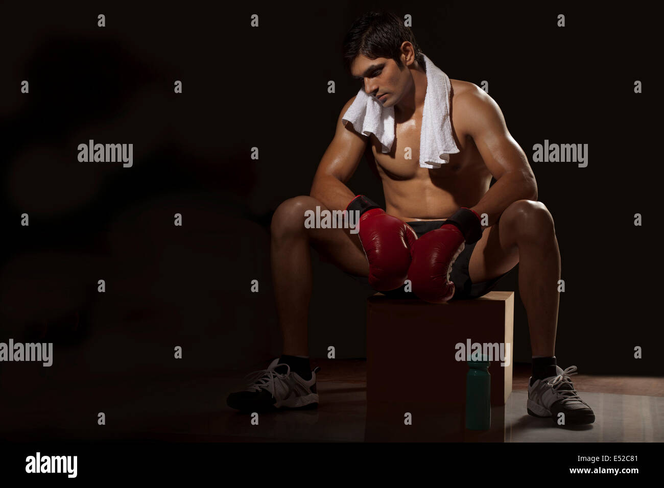Tired young man wearing boxing gloves resting on stool at gym Stock Photo