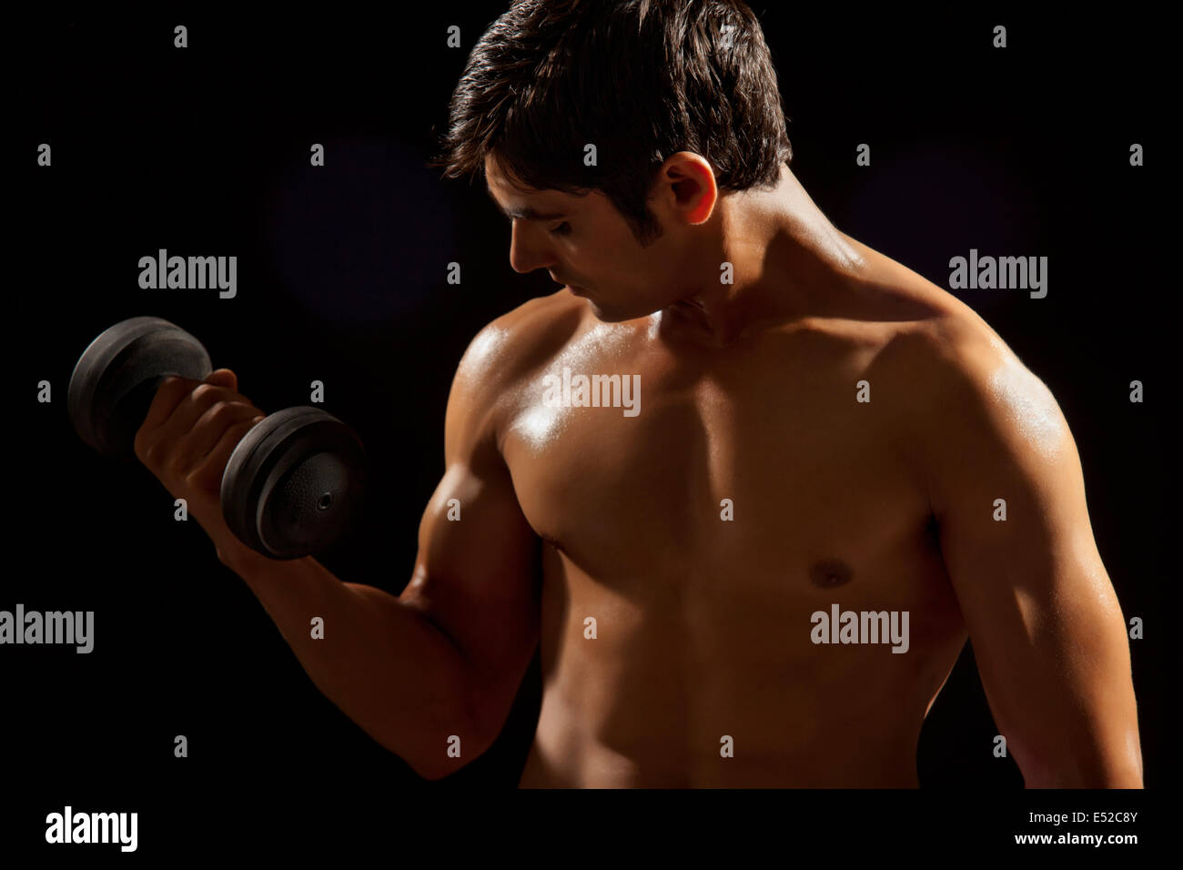 Young man exercising with dumbbell against black background Stock Photo