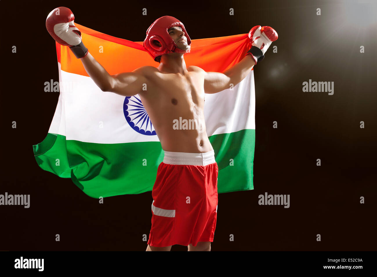 Successful male boxer looking up as he holds Indian flag isolated over black background Stock Photo