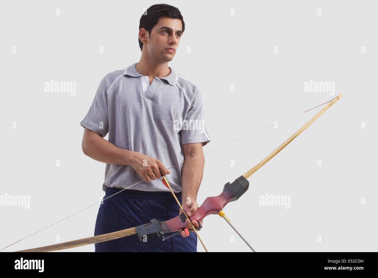 Young male archer with bow and arrow isolated over gray background Stock Photo