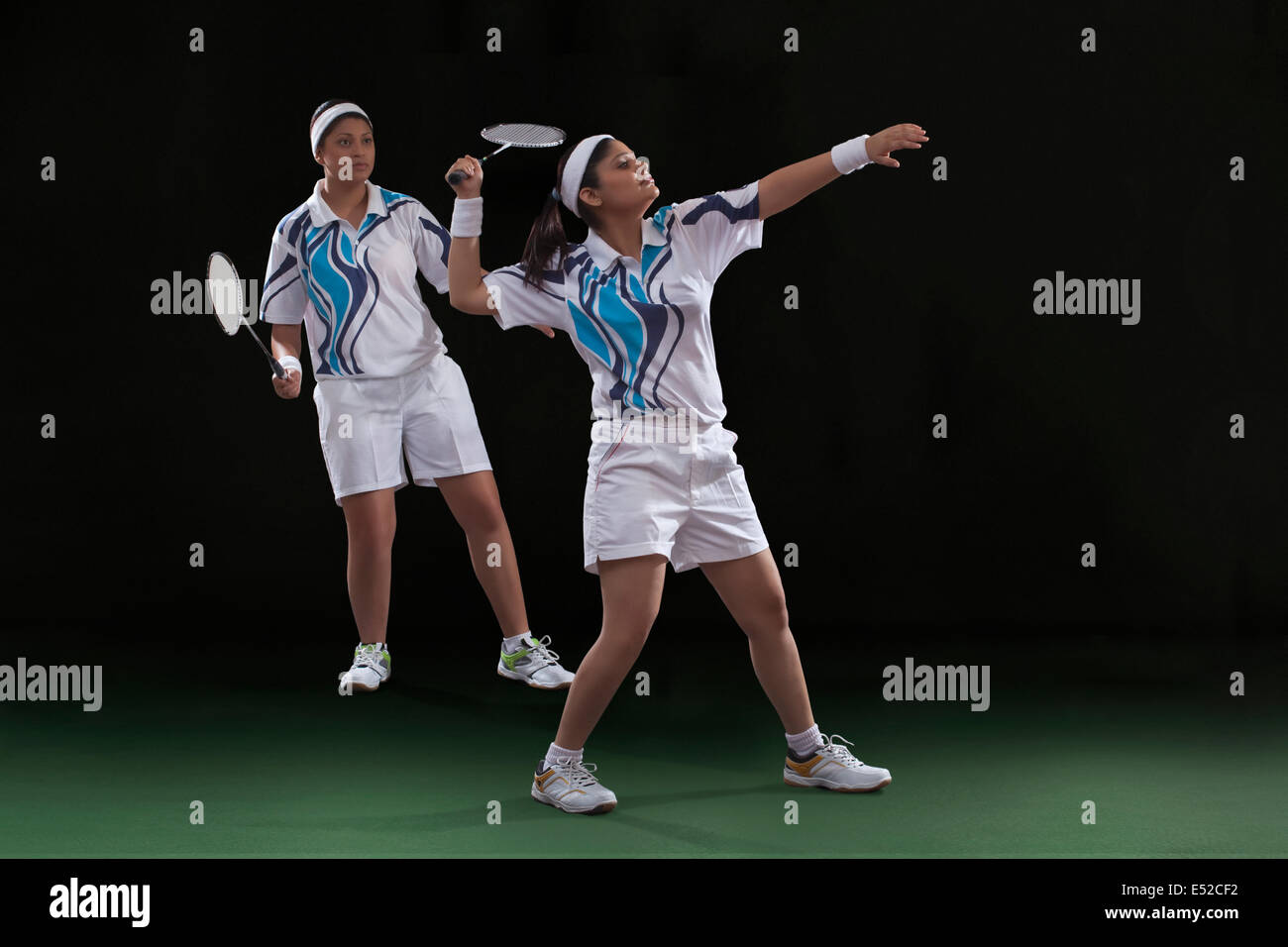 Young female players playing doubles badminton against black background Stock Photo