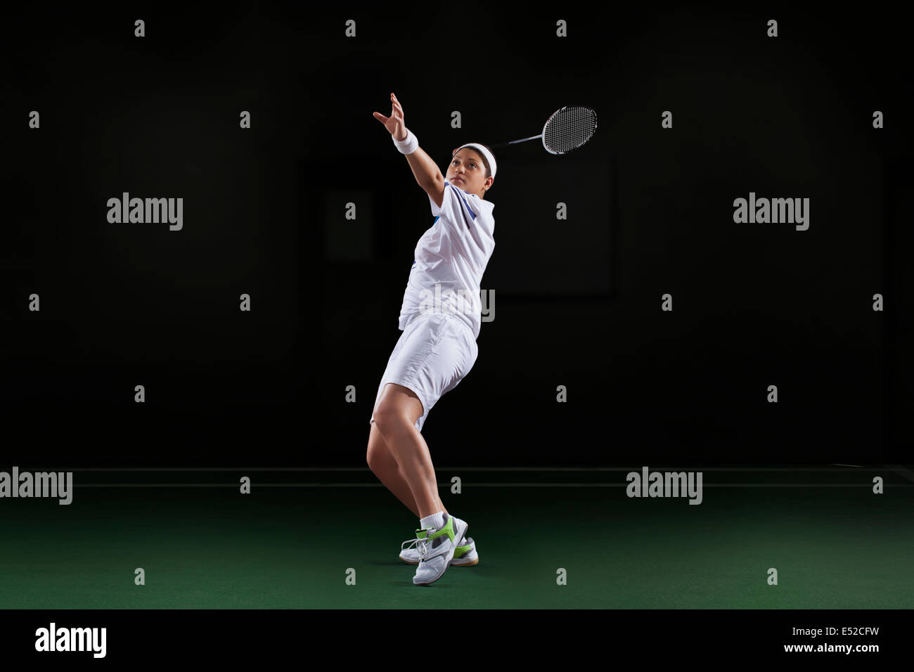 Side view of young woman in sportswear playing badminton isolated over black background Stock Photo