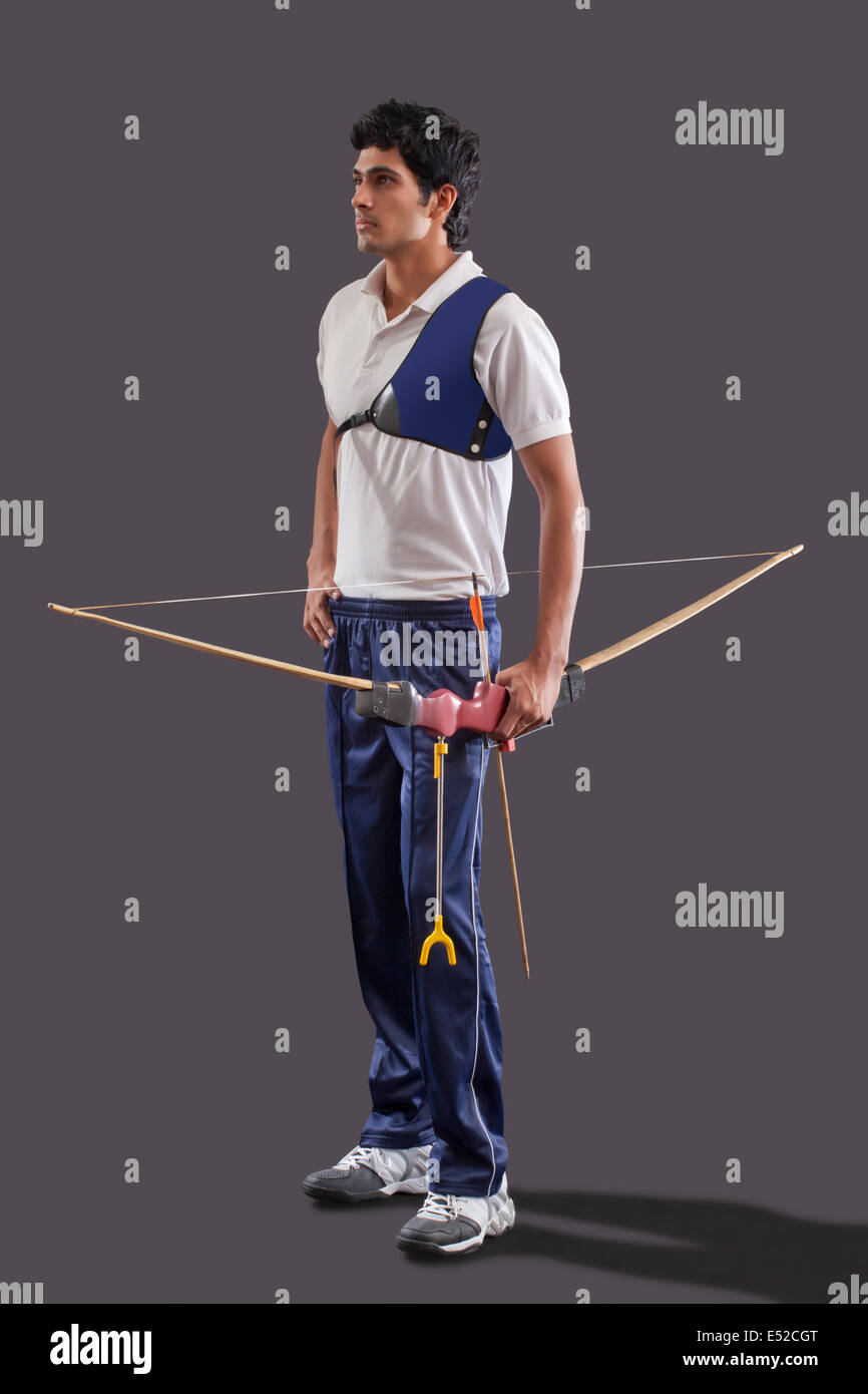 Full length of male archer with bow and arrow against gray background Stock Photo