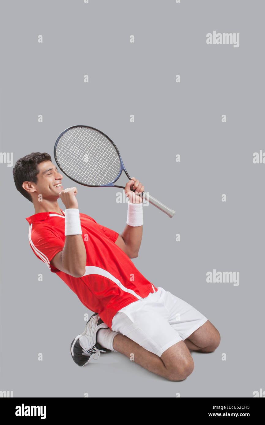 Happy male tennis player celebrating success over gray background Stock