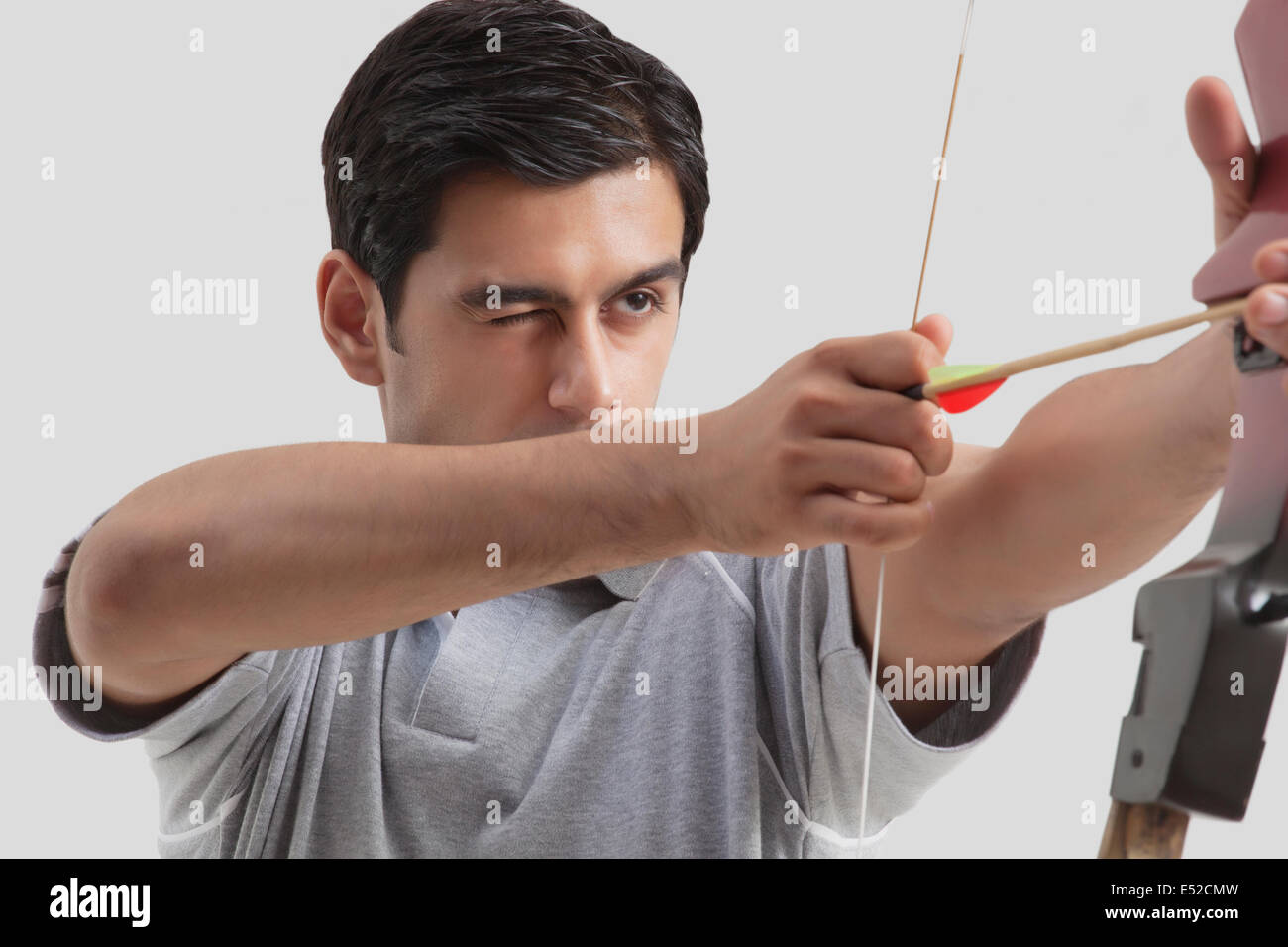 Male archer aiming bow and arrow isolated over gray background Stock Photo