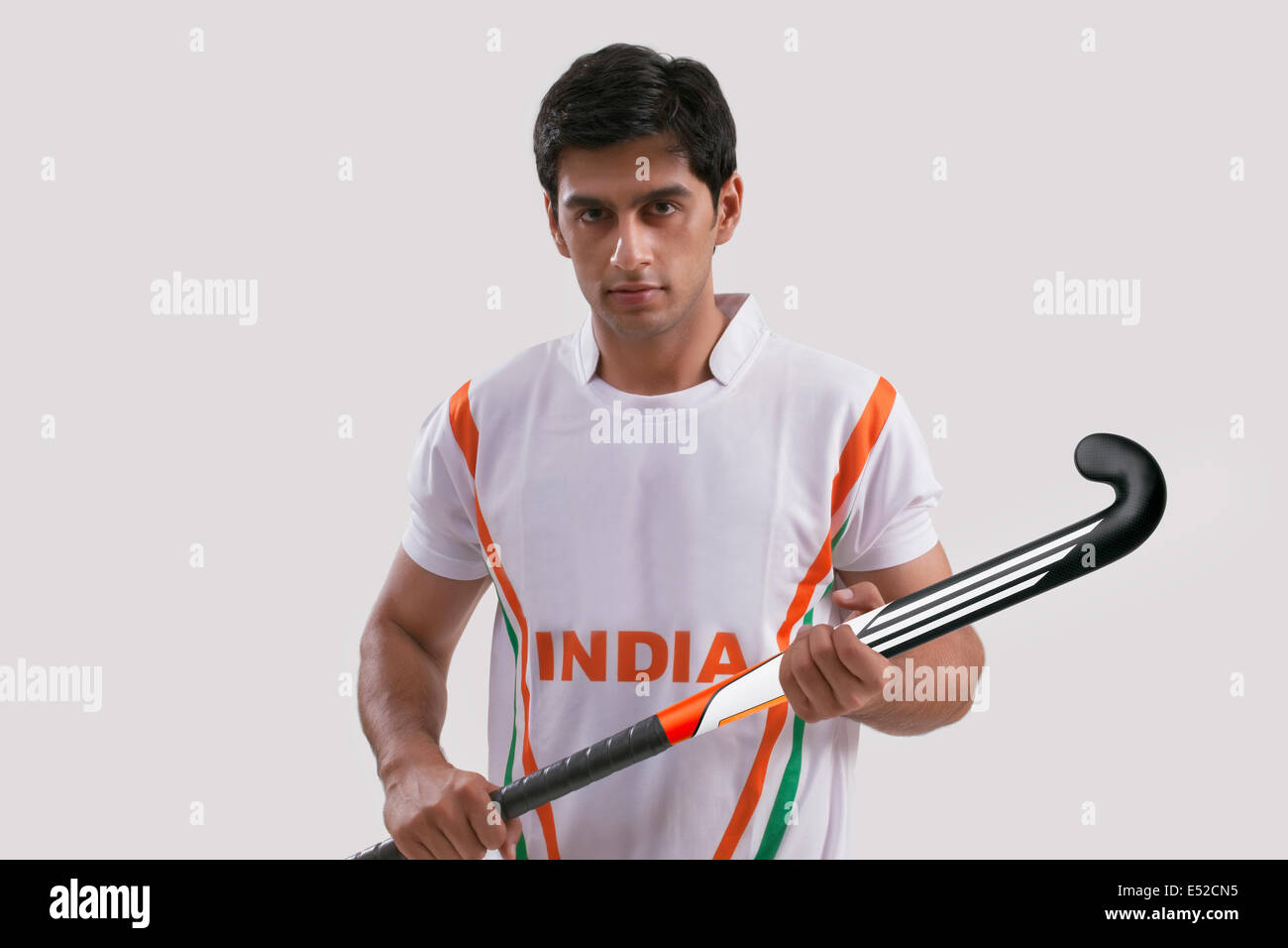 Portrait of young man holding hockey stick isolated over gray