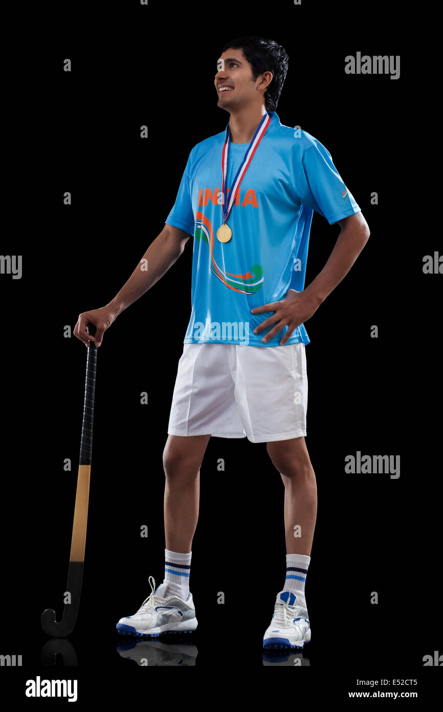 Confident young male winner with hockey stick looking up isolated over black background Stock Photo