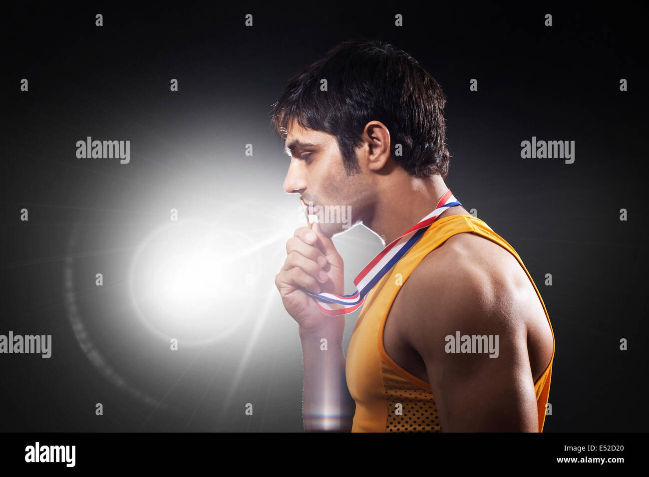 Close-up of young male runner kissing medal over black background Stock Photo