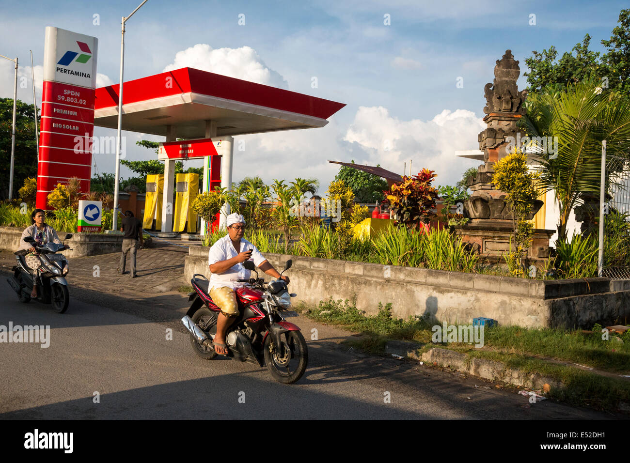 Bali, Indonesia.  Man Checking Cell Phone as he Drives Motorbike with One Hand.  No Helmet. Stock Photo