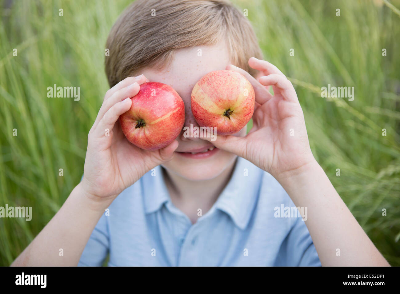 A boy holding two red skinned apples over his eyes. Stock Photo