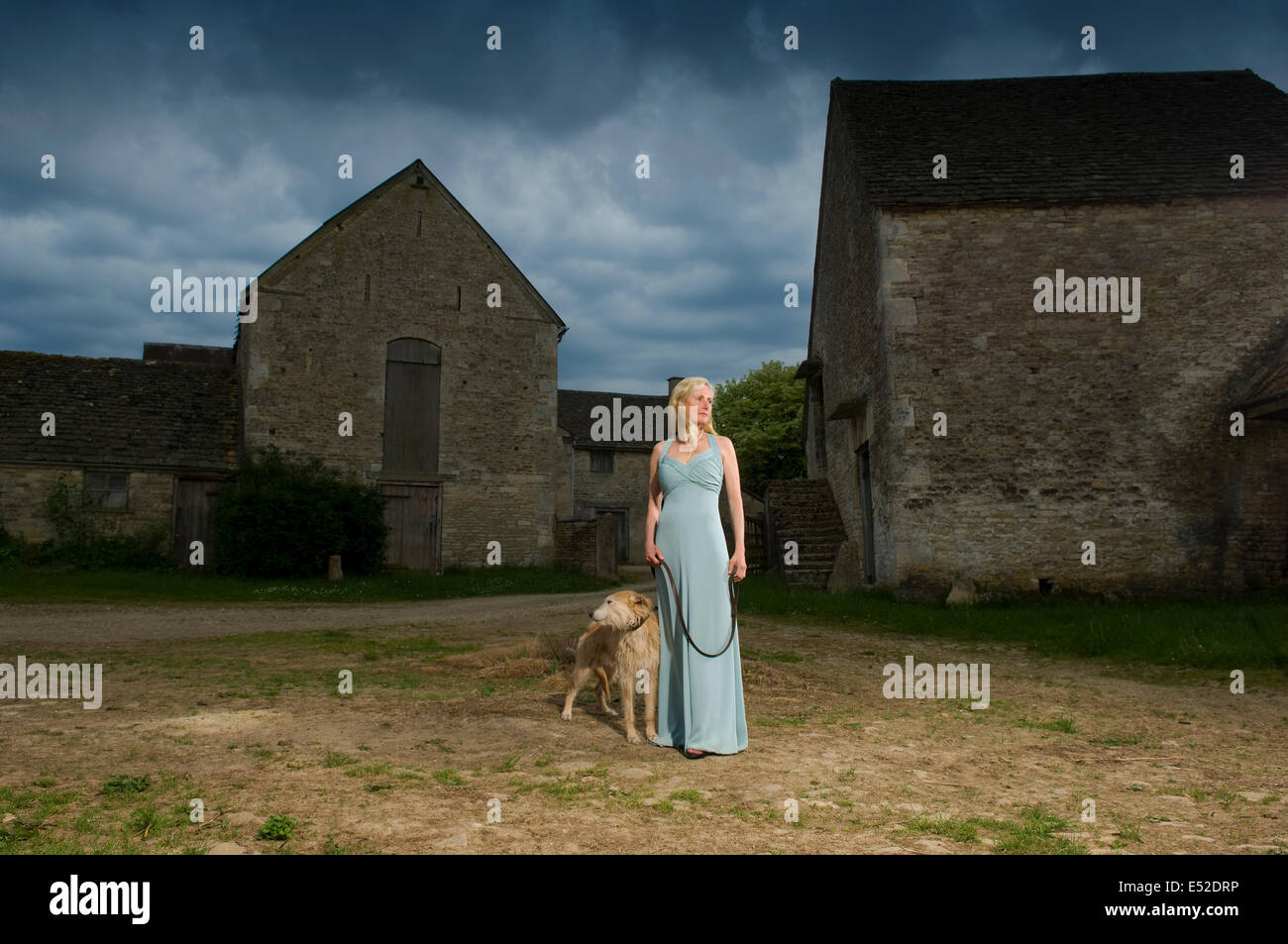 A woman with a lurcher dog in a farmyard, under a stormy sky. Stock Photo