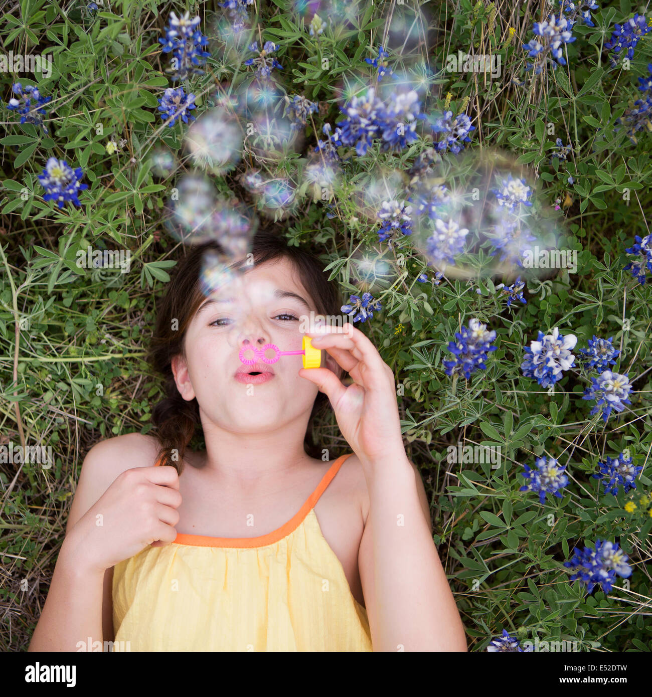 A girl lying on her back blowing bubbles in the air. Stock Photo