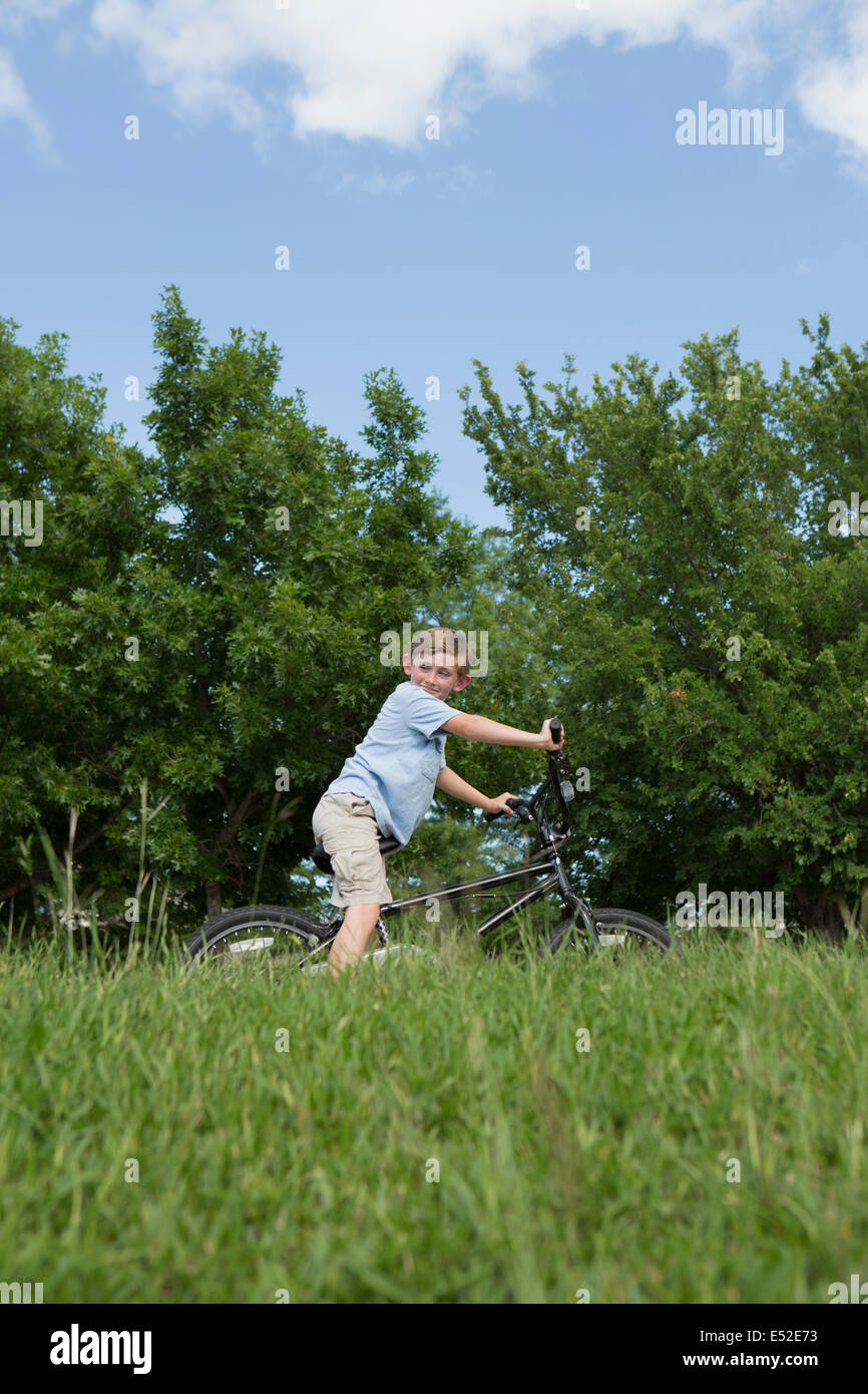 A young boy riding a bicycle through grass in a meadow. Stock Photo