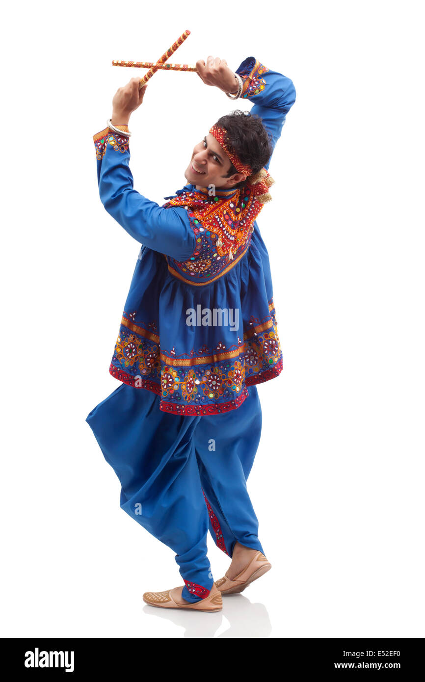 Portrait of happy young man in traditional clothes performing Dandiya ...