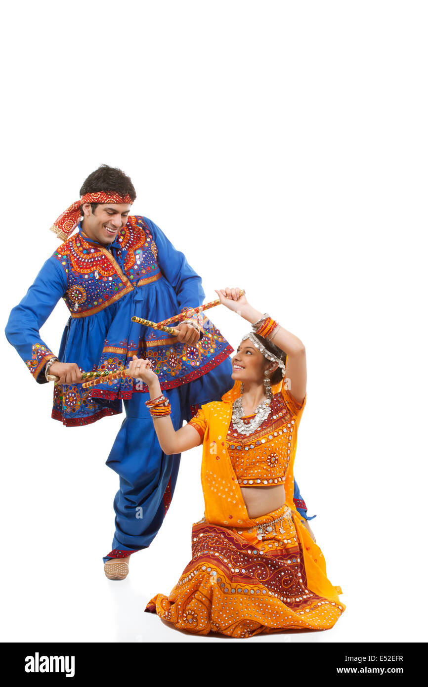 Happy young Indian couple performing Dandiya Raas over white background ...