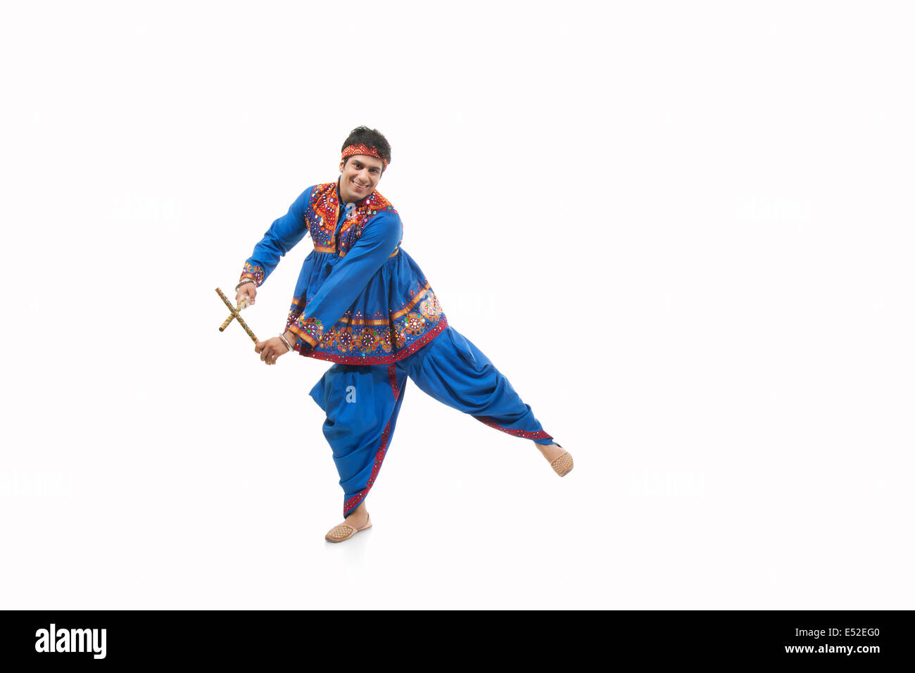 Portrait of happy young man in traditional wear performing Dandiya Rass ...