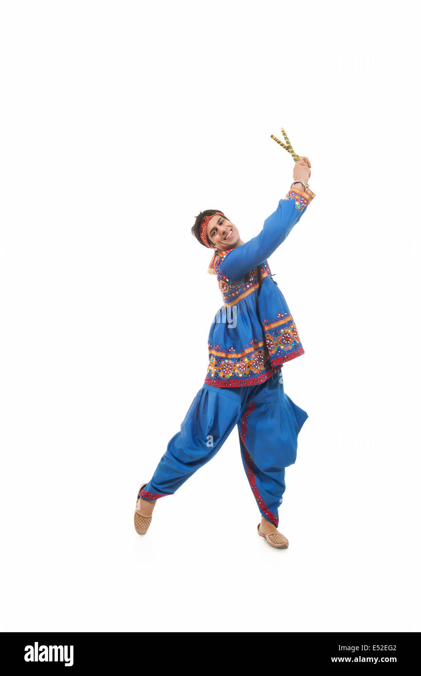 Portrait of happy young man in traditional clothes performing Dandiya ...
