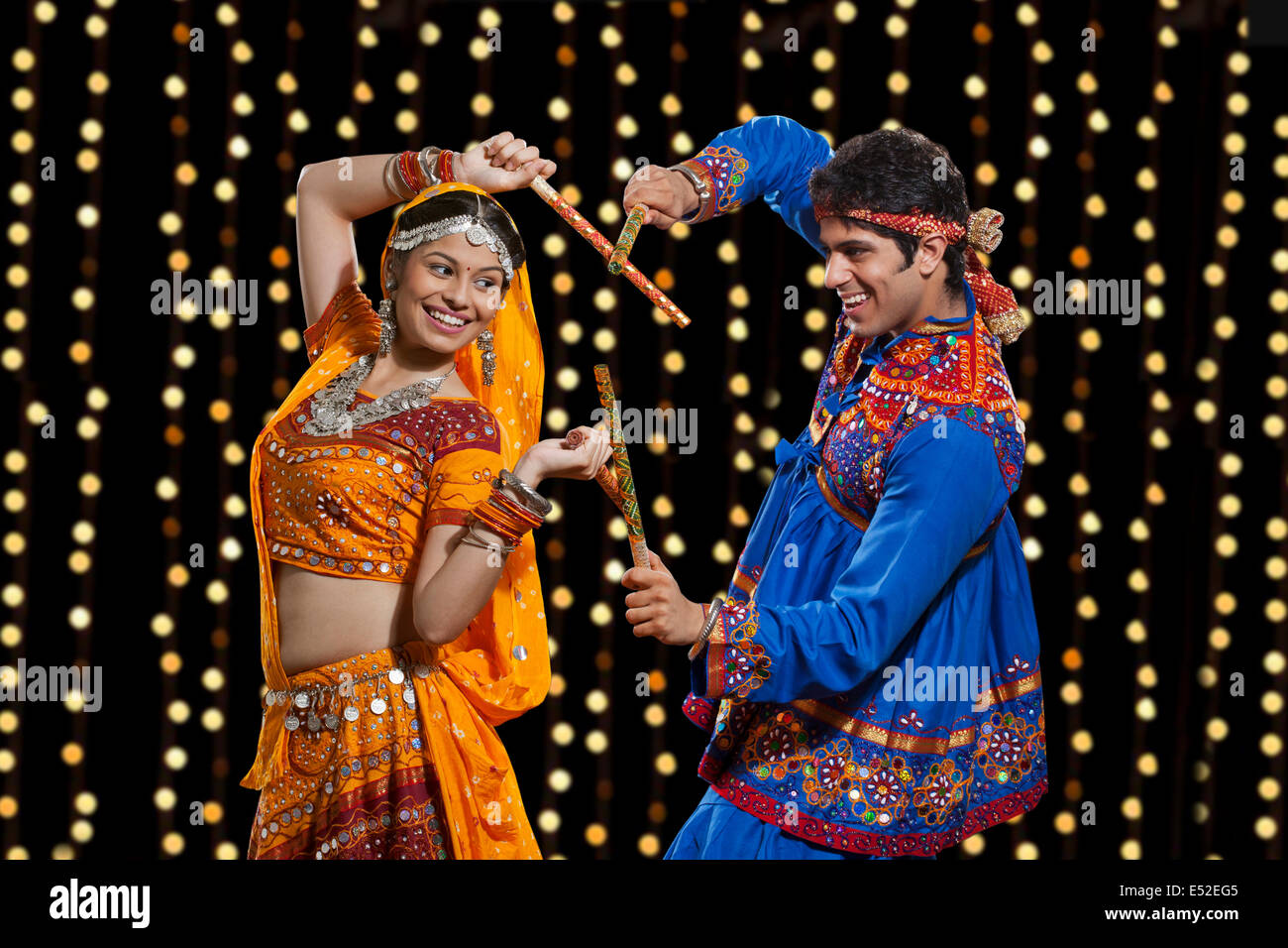 Happy young couple performing Dandiya Raas against neon lights Stock Photo