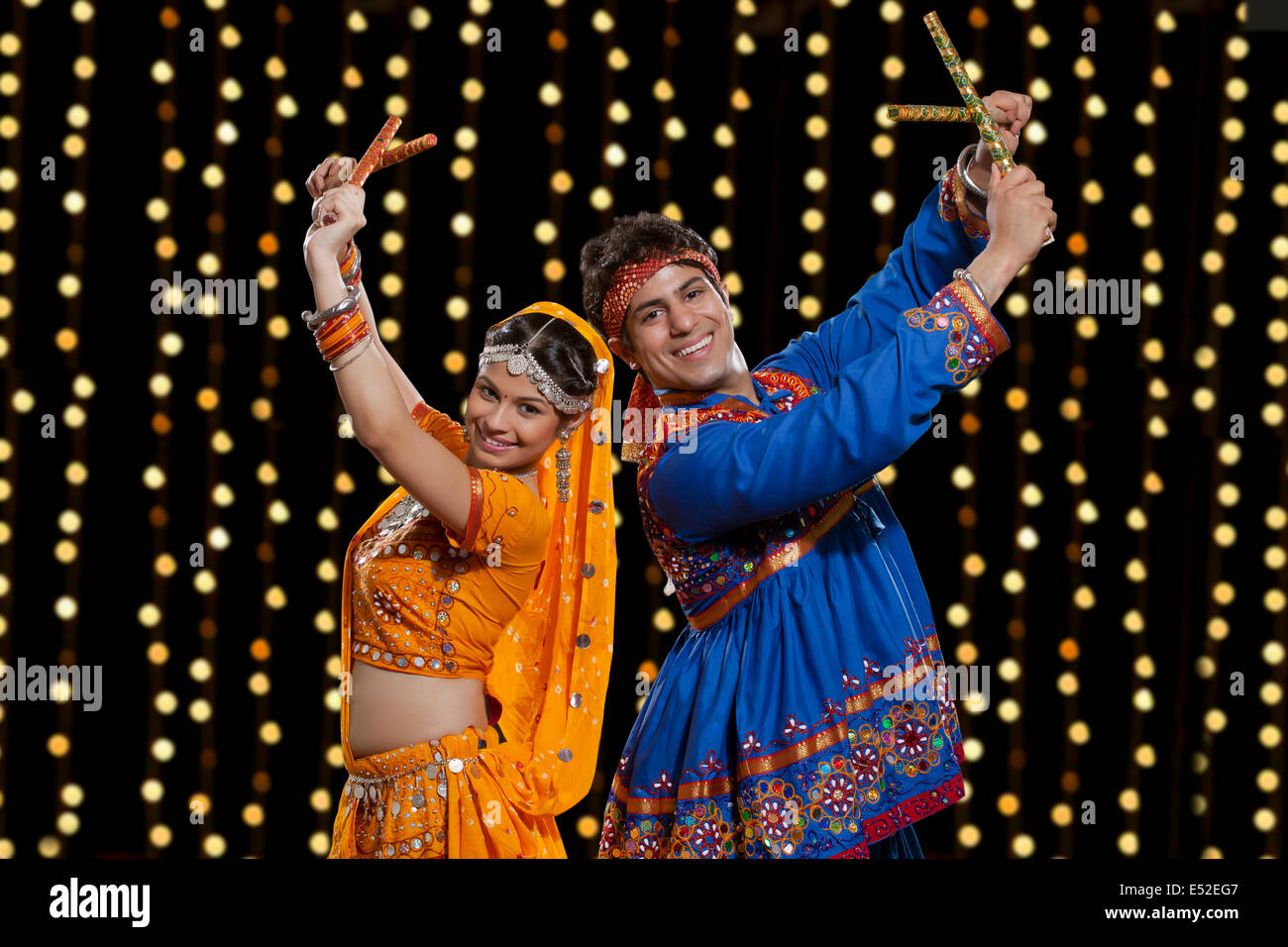Portrait of happy Indian couple in traditional wear performing Dandiya ...