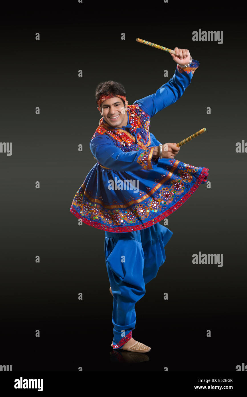 Full length portrait of man in traditional wear performing Dandiya Raas against black background Stock Photo