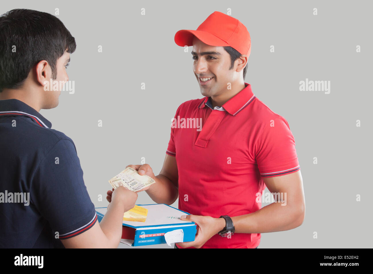 Young delivery man delivering pizza to customer over gray background