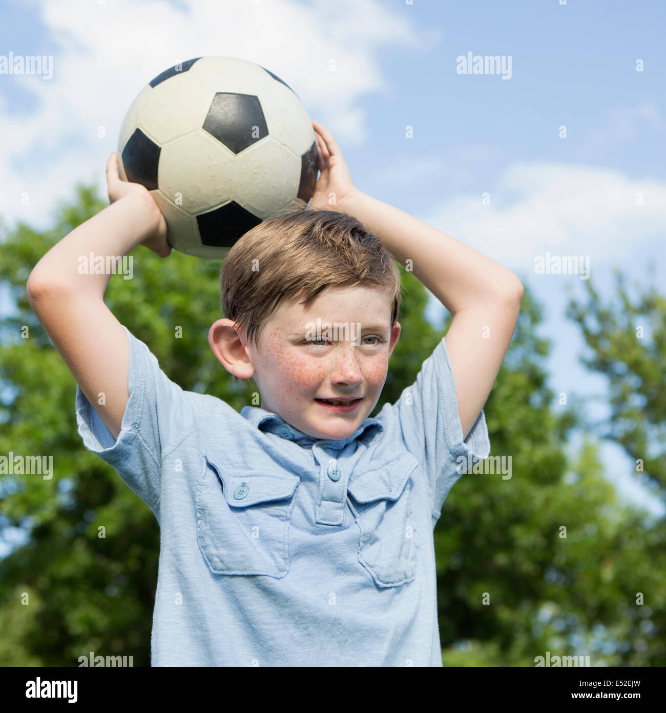 A young boy holding a soccer ball above his head. Stock Photo