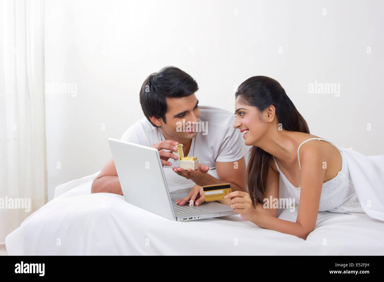 Young man opening ring box with woman shopping online with credit card in bed Stock Photo
