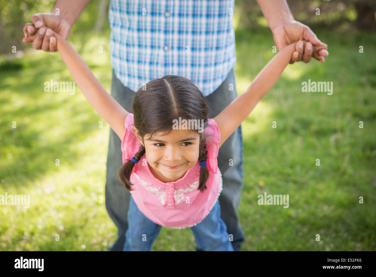 A young child in a pink dress with her arms outstretched playing with her father. Stock Photo