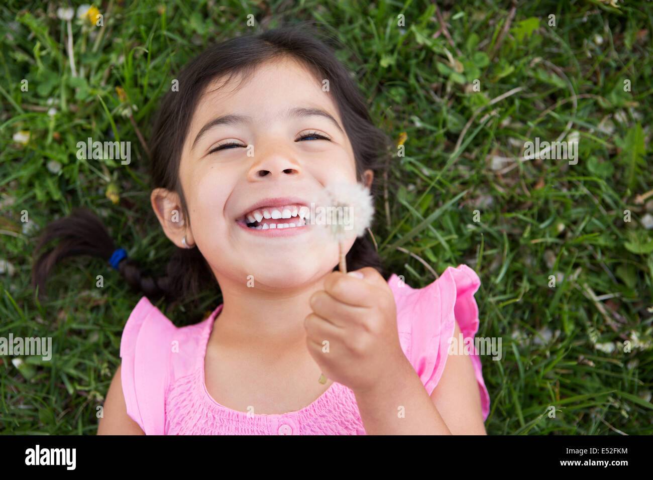 A girl lying on the ground, holding a dandelion seedhead clock. Stock Photo