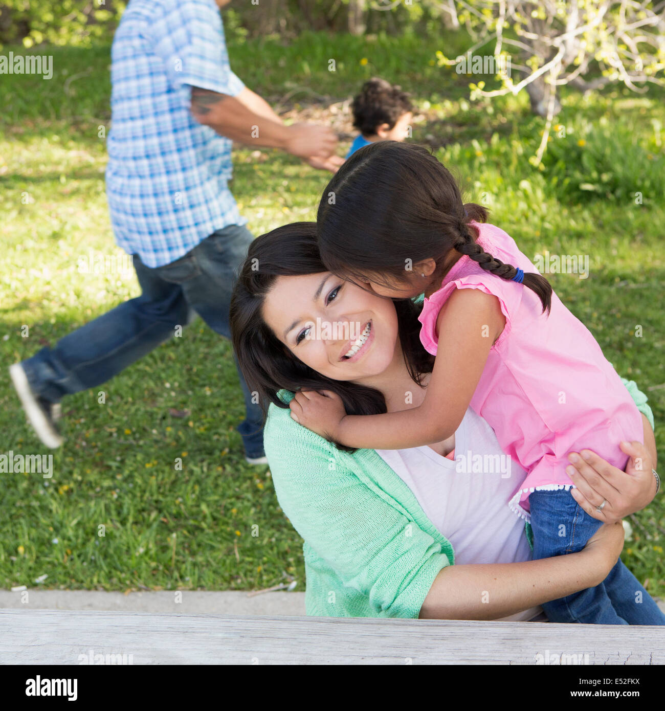 A mother in the park with her daughter, laughing and kissing each other. Father and son running on the grass. Stock Photo