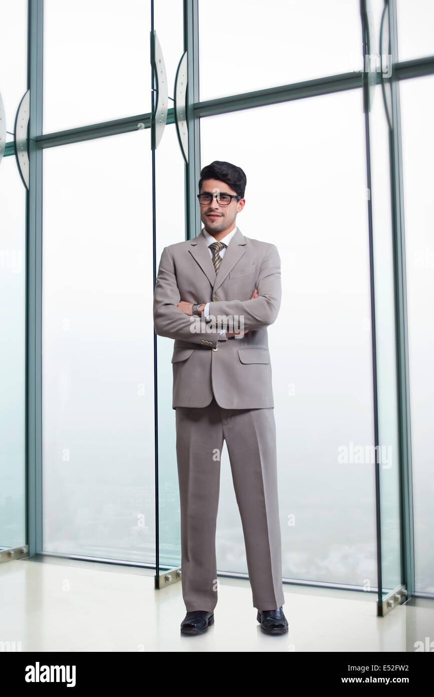 Full length portrait of businessman standing arms crossed in office ...