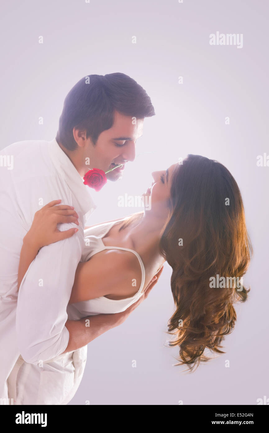 Romantic young man holding red rose in mouth while dancing with woman over  white background Stock Photo - Alamy