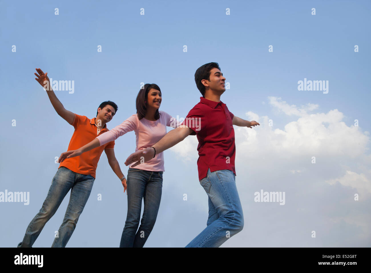 Low angle view of happy friends with arms outstretched against blue sky Stock Photo
