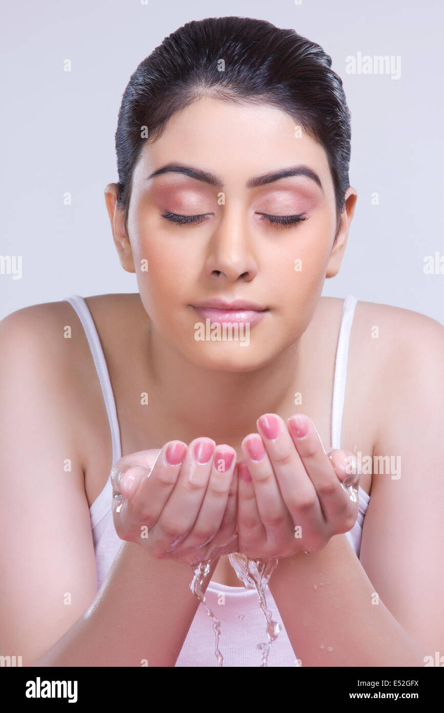 Beautiful woman washing face against gray background Stock Photo