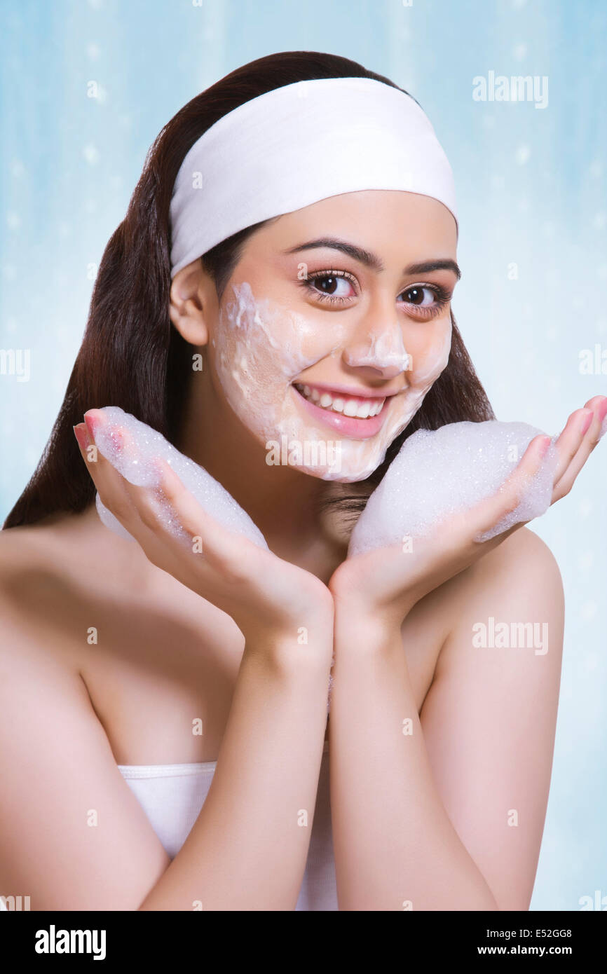 Portrait of beautiful woman washing face with soap against blue background Stock Photo
