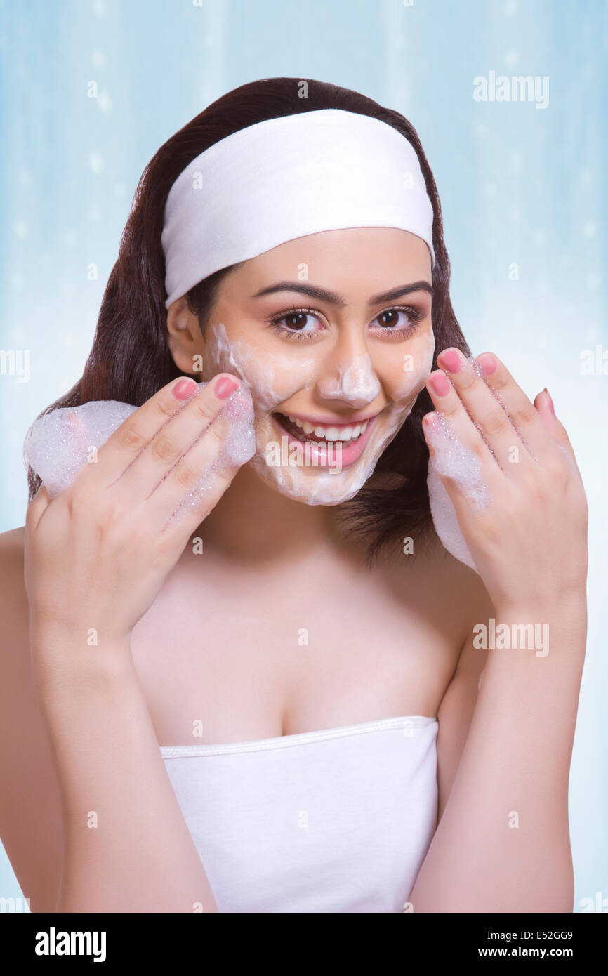 Portrait of beautiful woman scrubbing face with soap against blue background Stock Photo