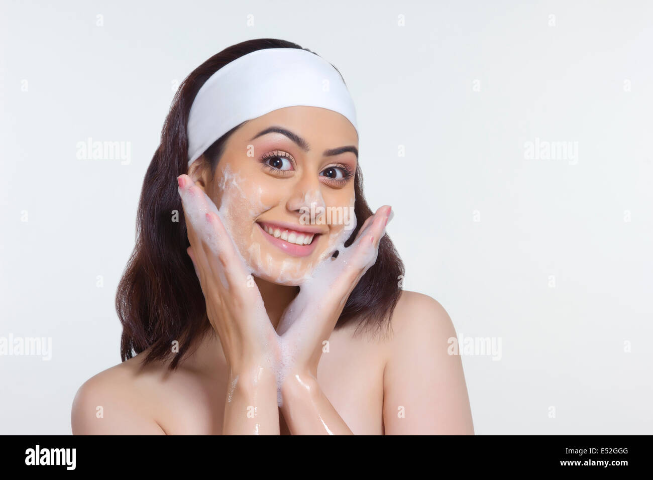 Portrait of beautiful woman scrubbing face with soap against white background Stock Photo