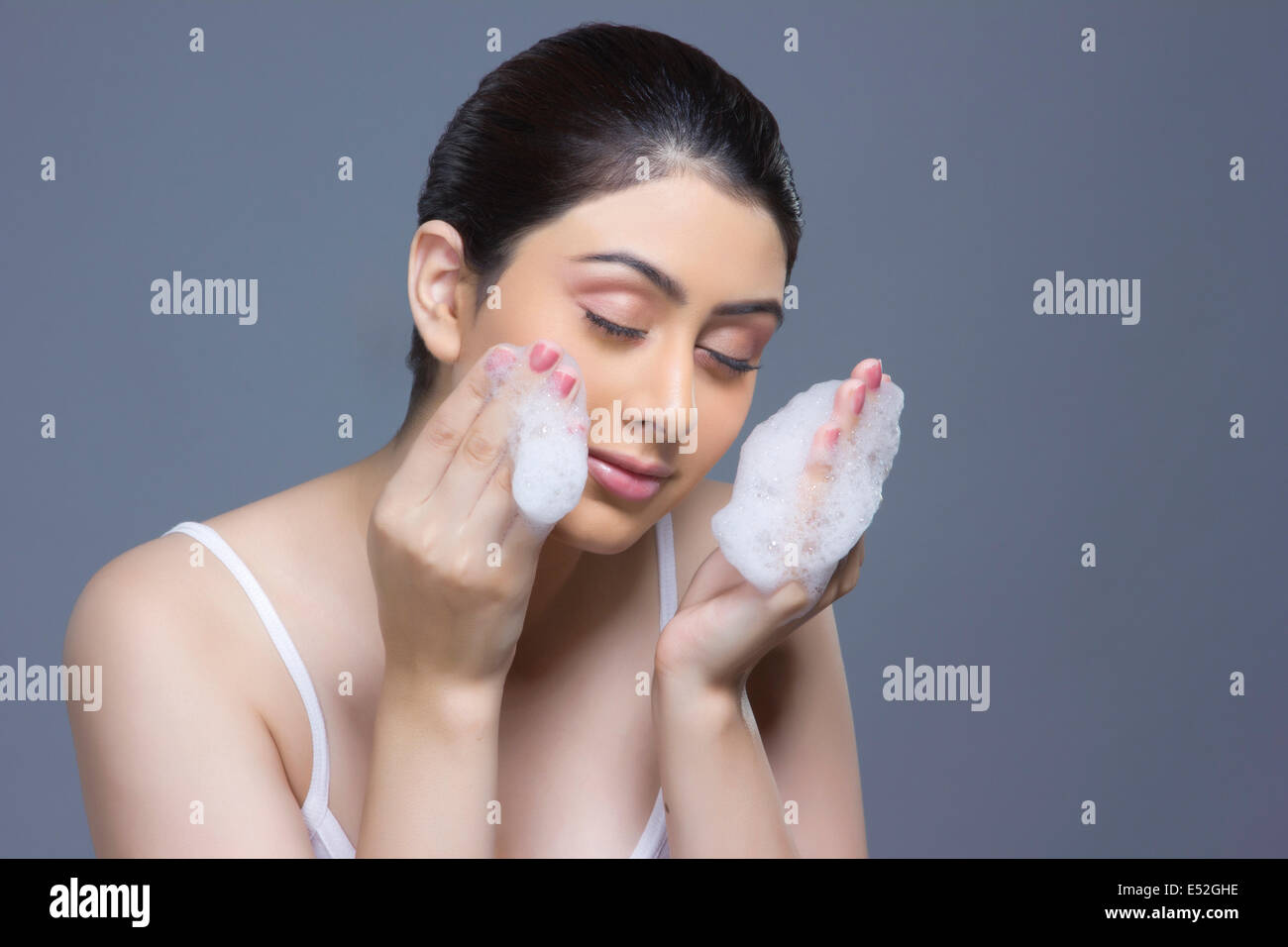 Beautiful woman washing face with soap sud against blue background