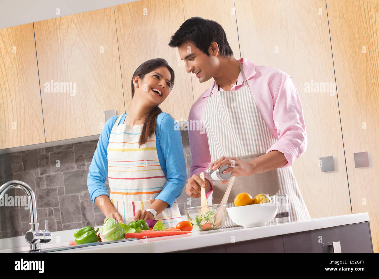 Happy young couple preparing fresh salad in kitchen Stock Photo