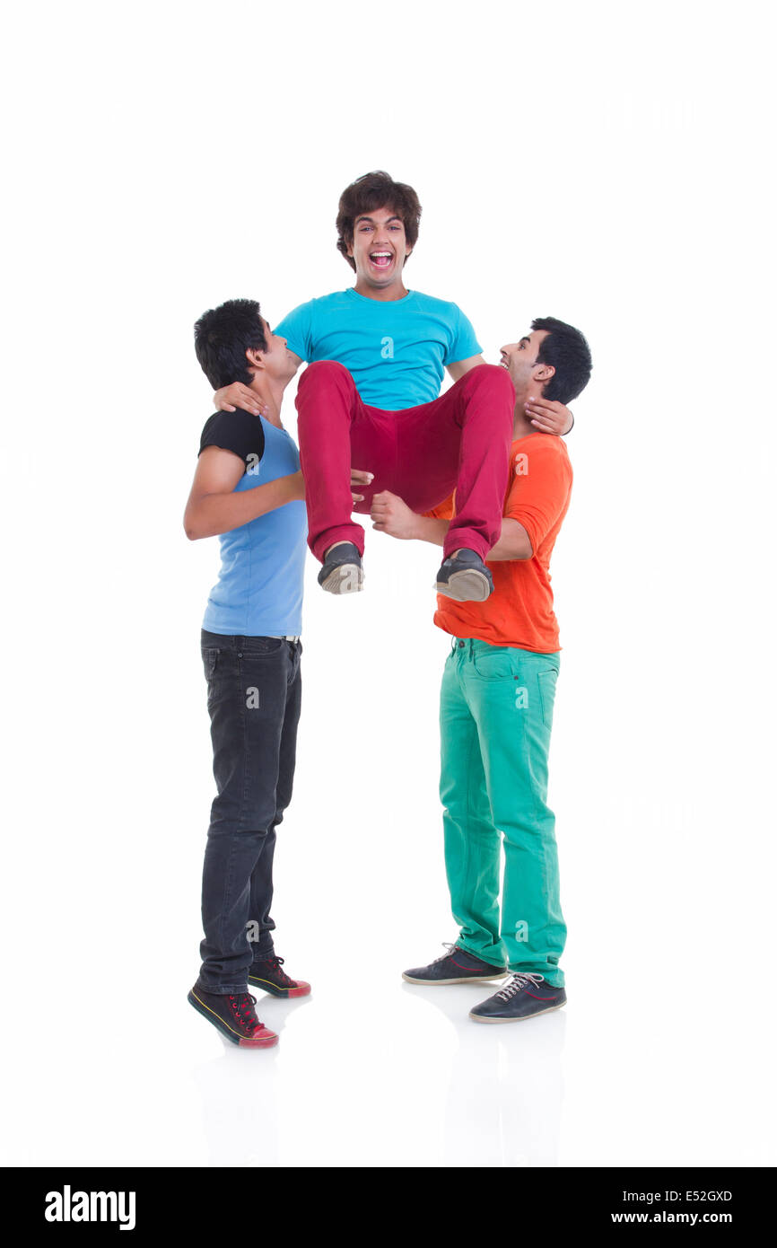 Full length of playful young men lifting male friend over white background Stock Photo